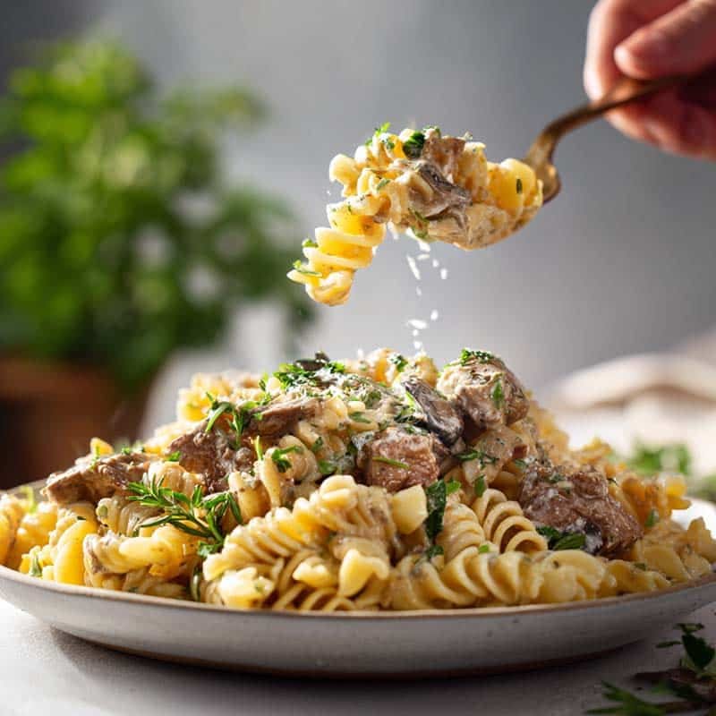 creamy beef pasta being plated with fresh parsley