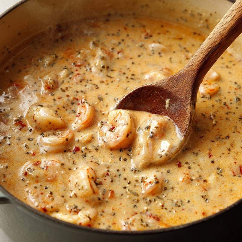 Mid-cook image showing seafood bisque in a pot, creamy texture with shrimp being stirred in, wooden spoon, slight steam