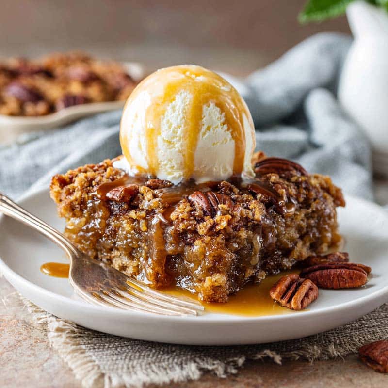 Slice of pecan pie dump cake with vanilla ice cream and caramel drizzle on white plate