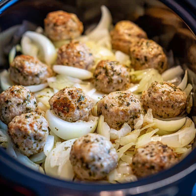 Slow cooker filled with onions and frozen meatballs