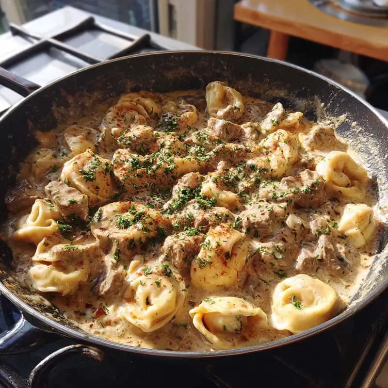 tortellini cooking in skillet with creamy beef stroganoff sauce
